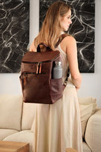All in One Leather Backpack in Chestnut worn by a woman in a cream dress with a bottle in the side pocket
