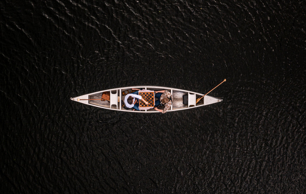 Leather Travel Chess Set, aerial view of two people playing chess on the board in a canoe on dark water