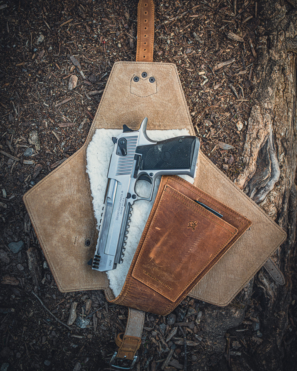 Leather Pistol Wrap in Tobacco unfolded on forest ground with a stainless pistol on the fleece lining