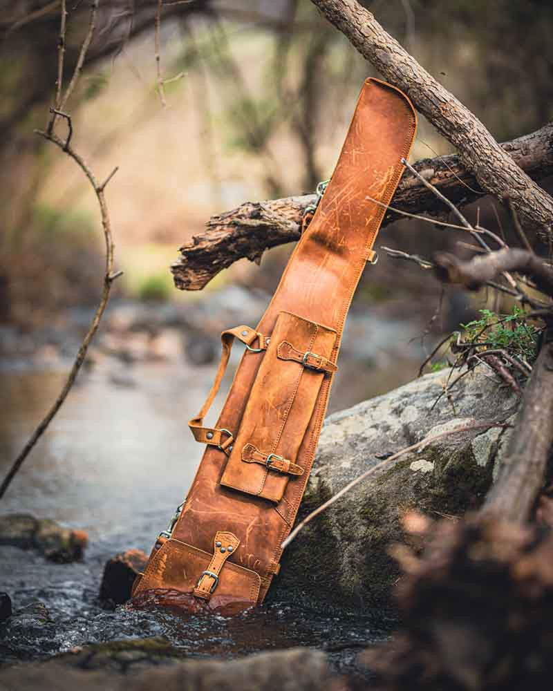 Shotgun Sleeve in Tobacco leaning against a mossy rock and branches in a shallow stream