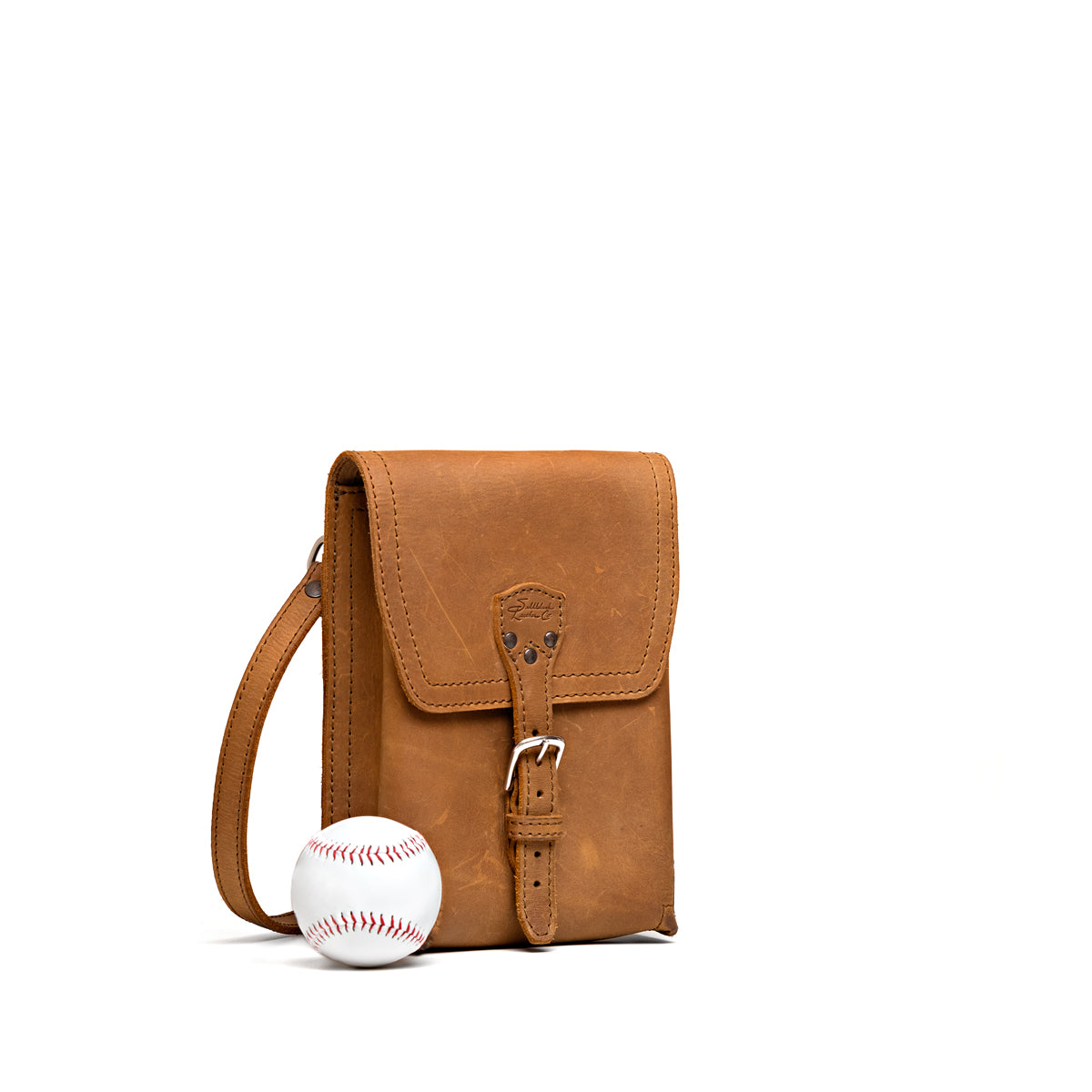 Leather Travel Satchel in Tobacco, angled front view with buckled flap, shown beside a baseball for size