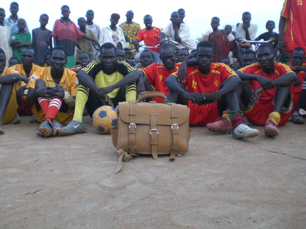 Large Classic Leather Briefcase in Tobacco on a dirt field in front of a seated soccer team and onlookers