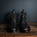 Officer's Boot in Raven Black, front view of the pair with shoe trees on a wooden table