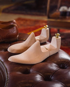 Shoe Tree pair in natural wood with brass knobs on a tufted leather ottoman