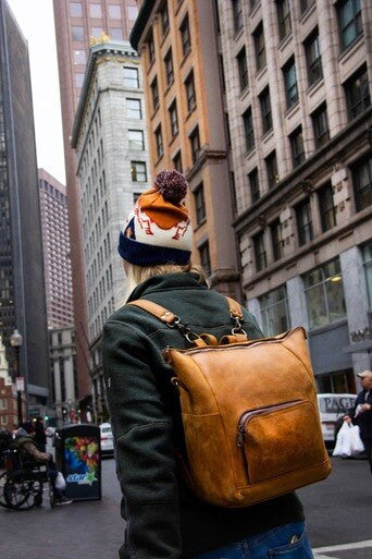 Universal Leather Backpack in Tobacco worn by a person in a beanie walking down a city street