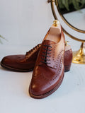 Wingtip Shoes in Chestnut, pair with shoe trees in front of a brass-framed mirror
