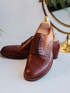 Wingtip Shoes in Chestnut, pair with shoe trees in front of a brass-framed mirror