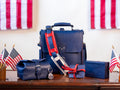 Saddleback Club Membership, navy blue leather bag and accessories with red straps displayed among American flags