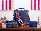 Saddleback Club Membership, navy blue leather bag and accessories with red straps displayed among American flags