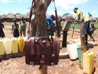 Large Classic Leather Briefcase in Chestnut hanging on a tree at a village water pump with people and water jugs