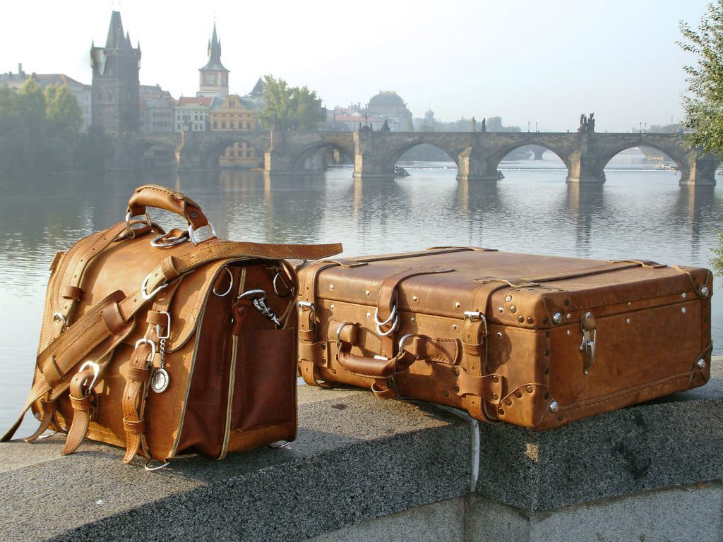 Large Classic Leather Briefcase in Tobacco beside a leather suitcase on a riverside ledge facing a historic stone bridge