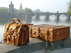 Large Classic Leather Briefcase in Tobacco beside a leather suitcase on a riverside ledge facing a historic stone bridge