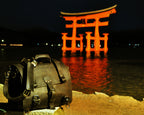 Large Classic Leather Briefcase in Dark Coffee Brown on a rocky shore at night before a lit red torii gate in the water