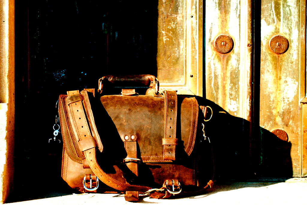 Large Classic Leather Briefcase in Tobacco lying on its side in sunlight before weathered riveted metal doors