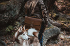 Slim Leather Briefcase in Chestnut carried by a person in a leather jacket on a forest trail beside a husky