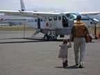 Tank Backpack in Tobacco, worn by a man walking with a small child toward a bush plane