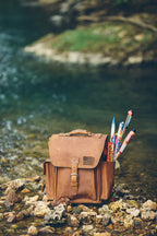 Tank Backpack in Tobacco with an American flag patch, filled with fireworks on a rocky stream bank