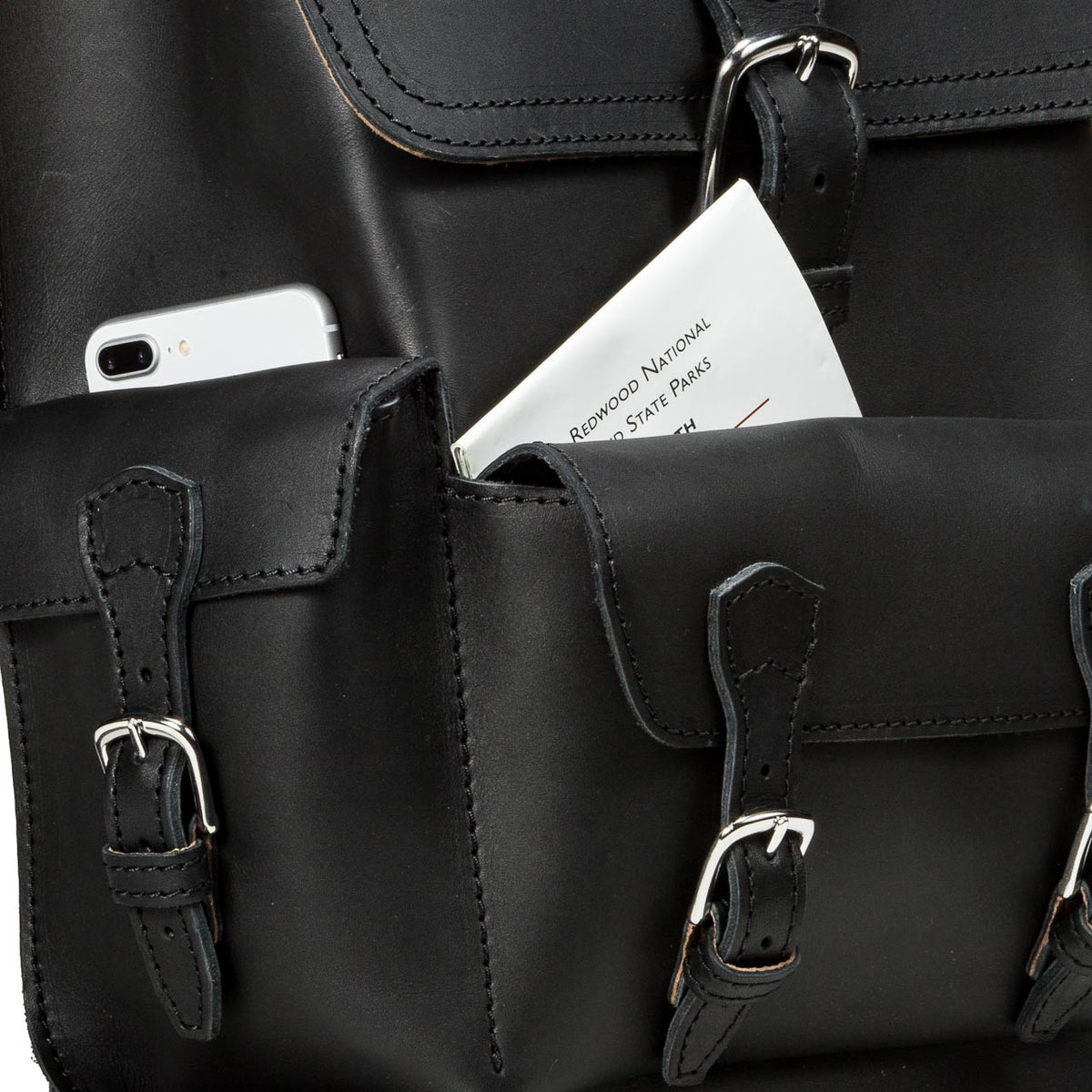 Thin Front Pocket Leather Backpack in Black, close-up of front pockets holding a phone and a park map