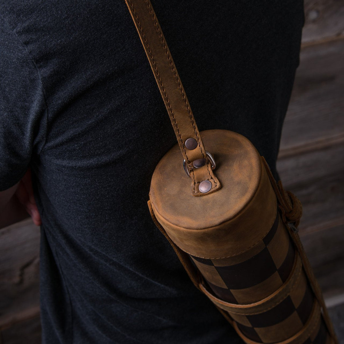 Leather Travel Chess Set in Tobacco, close-up of rolled checkerboard case with riveted strap carried on a man's shoulder