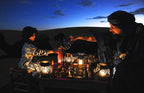 Leather Travel Chess Set with pieces on a lantern-lit table in the desert at dusk as two people share tea