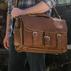 Front Pocket Leather Briefcase in Tobacco held by the top handle by a person in a plaid flannel shirt and jeans