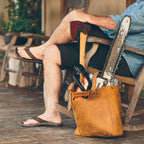 Everyday Leather Tote in Tobacco on a porch holding an axe, chainsaw and hand tools beside a man in a rocking chair