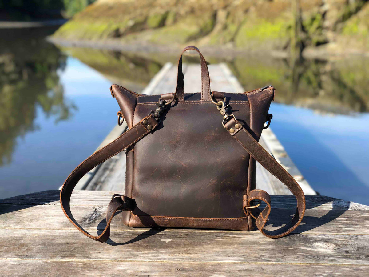 Universal Leather Backpack in Dark Coffee Brown, back view with shoulder straps on a lakeside dock