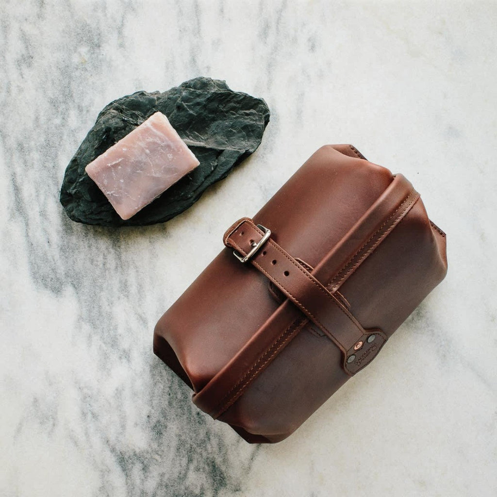 Big Mouth Leather Toiletry Bag in Chestnut on a marble counter beside a bar of soap on a slate dish