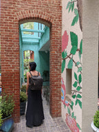 All in One Leather Backpack in Black worn by a woman walking through a brick archway beside a floral mural