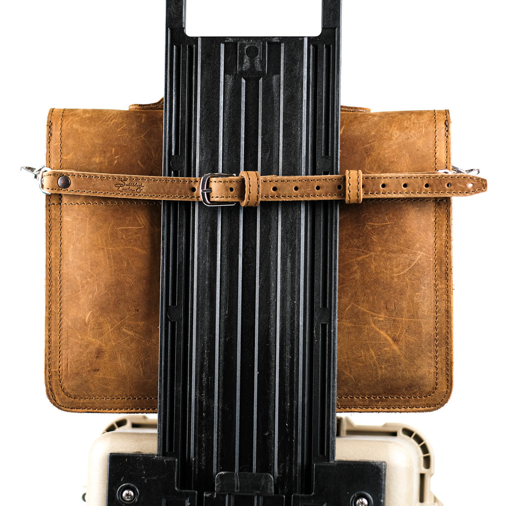 Leather Luggage Strap in Tobacco buckled around a leather bag to secure it to a rolling suitcase handle