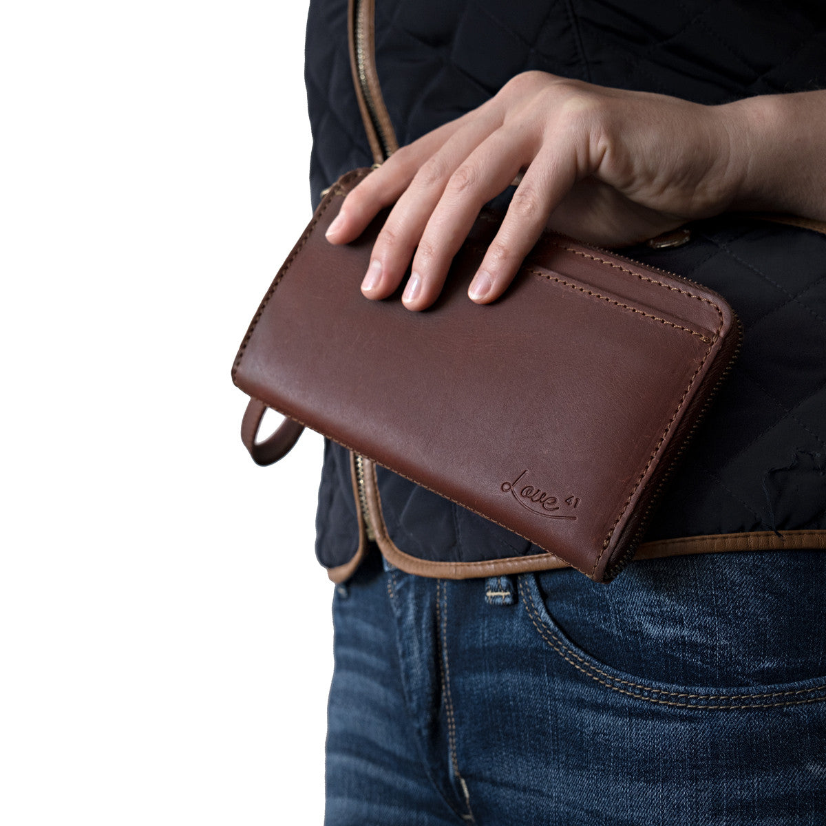 Medium Wristlet Leather Wallet in burgundy brown, held against a quilted vest and jeans