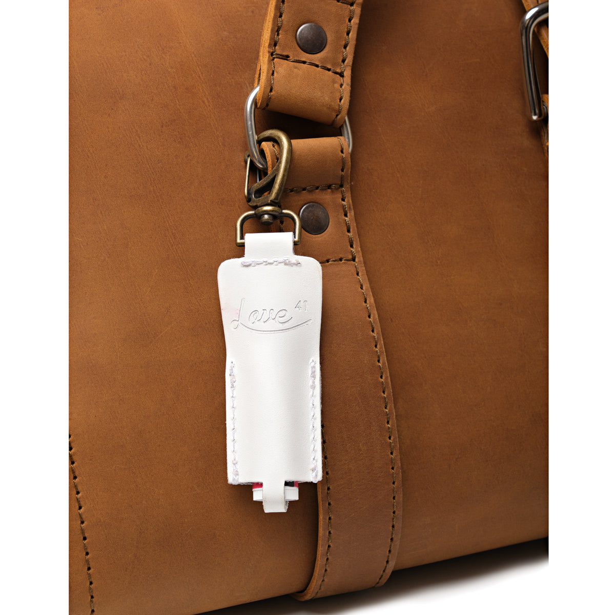 Leather Chapstick Holder in white, clipped to the strap ring of a tan leather bag