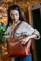 Concealed Carry Leather Tote in Chestnut, woman reaching into the side carry compartment while wearing the tote
