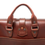 Flight Bag Leather Briefcase in chestnut, close-up of the top handle and riveted tab with embossed Saddleback Leather Co. logo