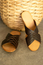 Martha Sandals in Dark Coffee Brown, one propped against a woven basket on a stone floor