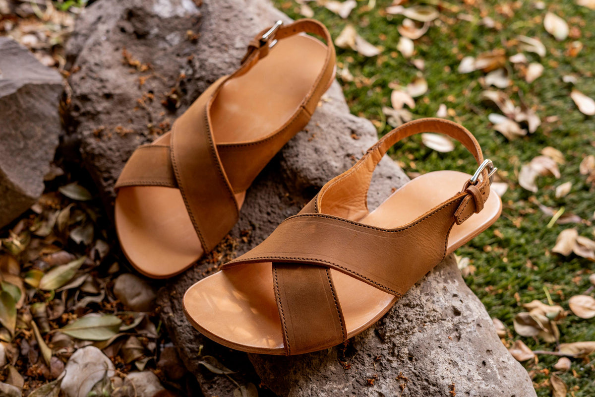 Pair of Jesus Sandals in Tobacco leather resting on a gray rock among fallen leaves and grass