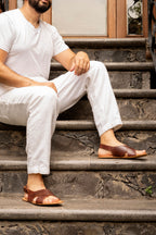 A man in white sitting on stone steps wearing Jesus Sandals in Chestnut leather