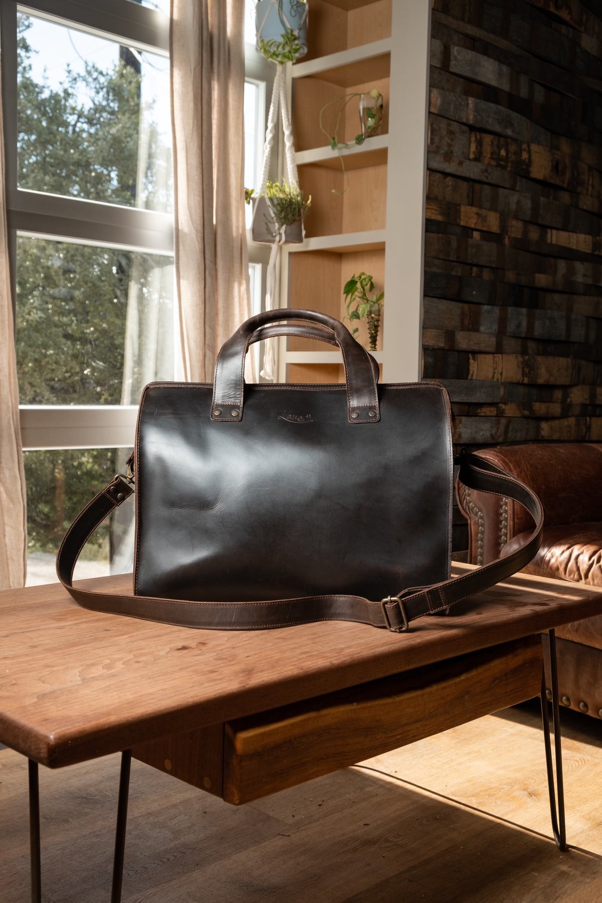 Simple Overnight Leather Duffle Bag in Dark Coffee Brown, sitting on a wooden table by a sunny window