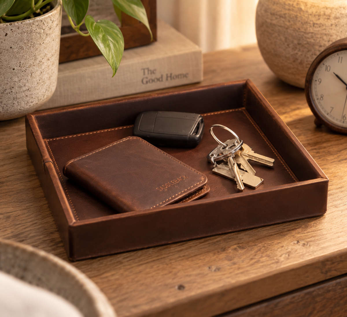 The Simple Leather Valet Tray in Dark Coffee Brown with a wallet, key fob and keys on a wooden dresser beside a clock