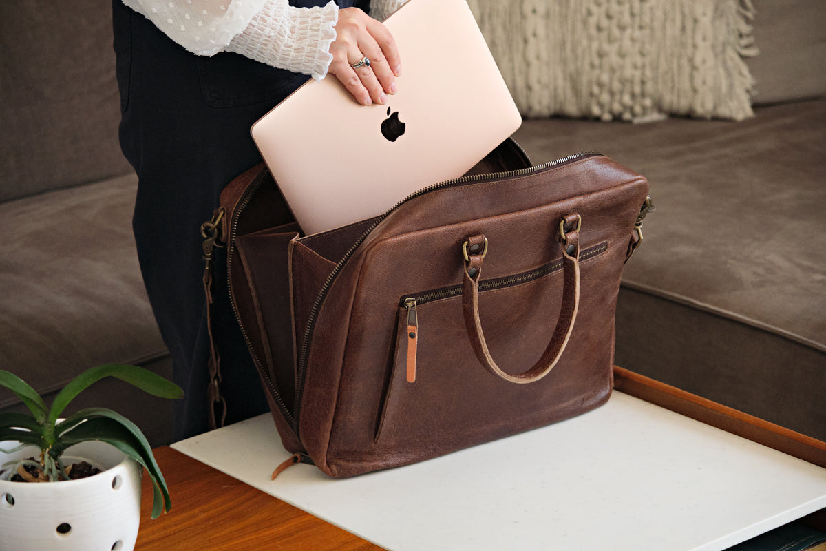 Women's Business Satchel in Chestnut, unzipped as a woman slides a laptop into the main compartment