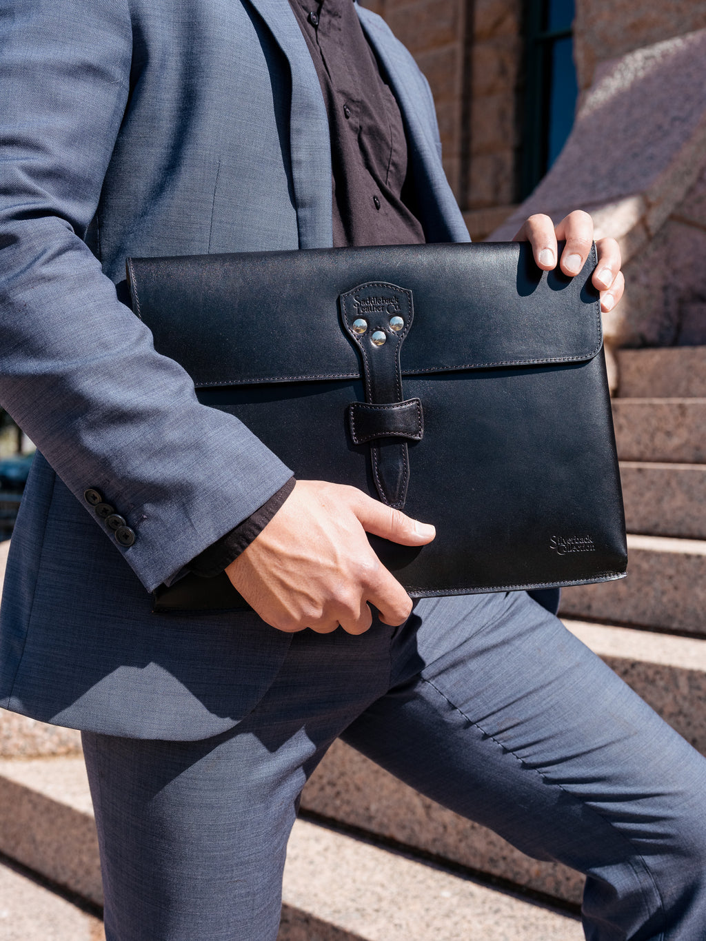 Silverback Document Holder in Black, carried under the arm by a man in a blue suit on stone steps