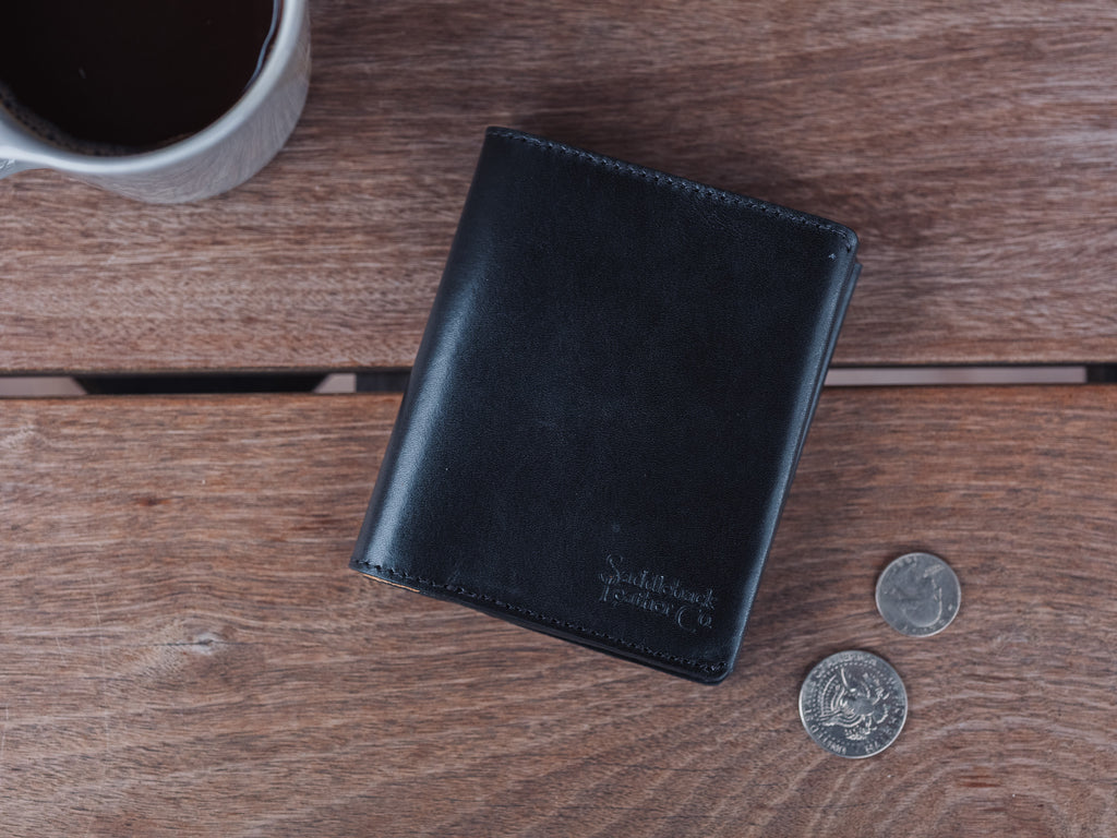Large Bifold Wallet in Raven Black on a wooden table next to two coins and a coffee mug