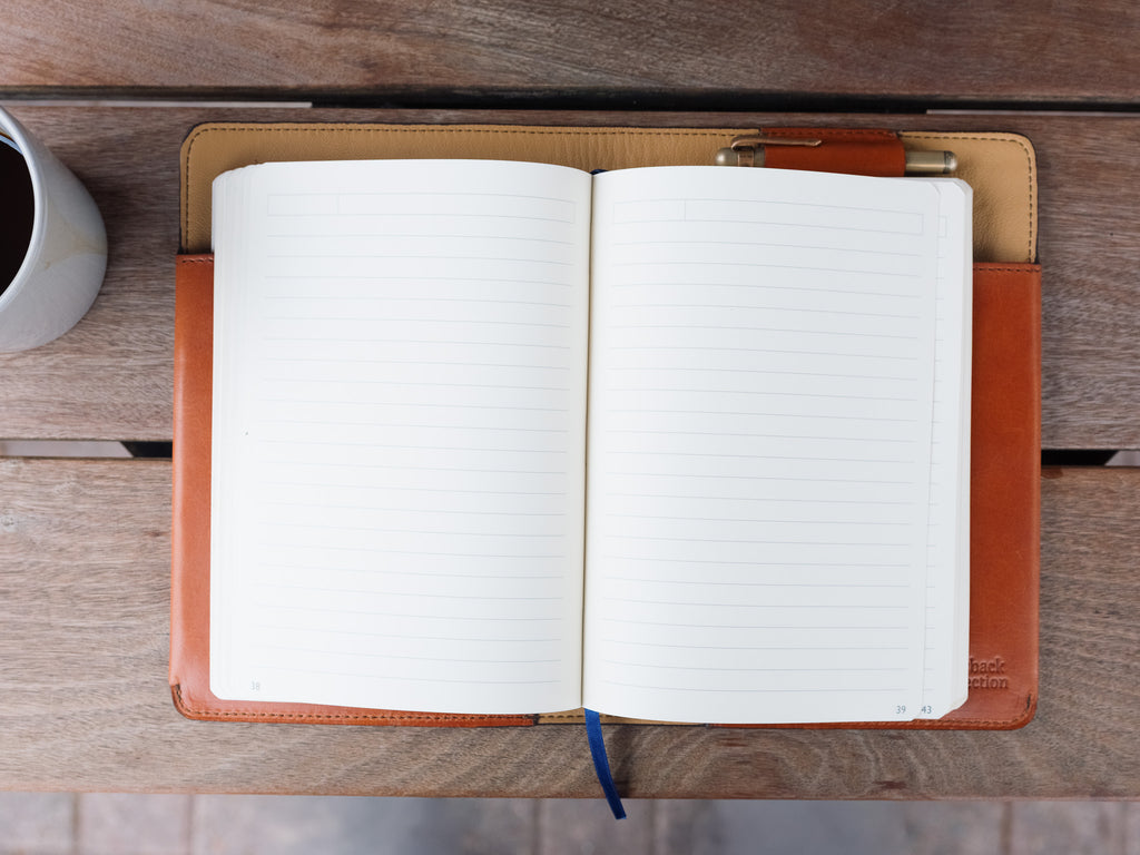 J.R.R. Tolkien Journal Cover in English Tan holding an open lined notebook and pen, beside a coffee mug
