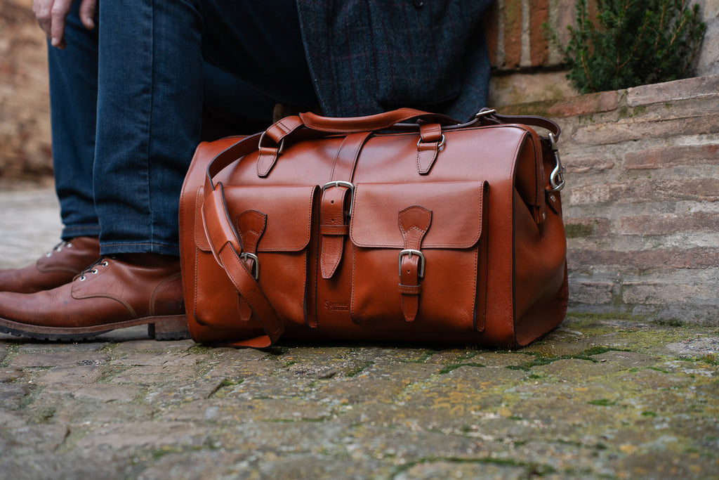 Wesley Deep Pocket Duffle in English Tan on a stone street beside brown leather boots