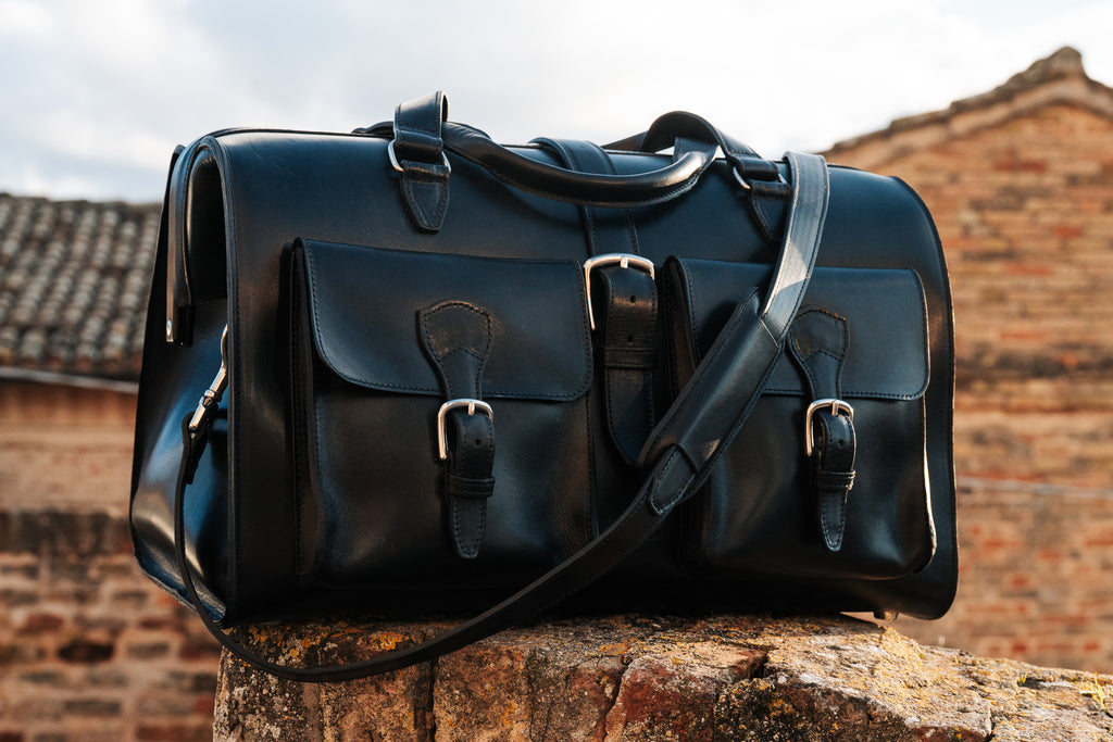 Wesley Deep Pocket Duffle in Raven Black on a stone ledge in front of brick buildings