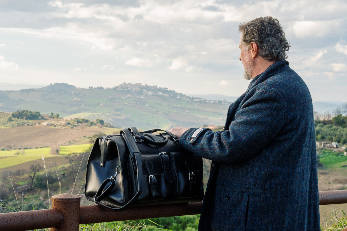 Wesley Deep Pocket Duffle in Raven Black on a fence rail beside a man overlooking the hills