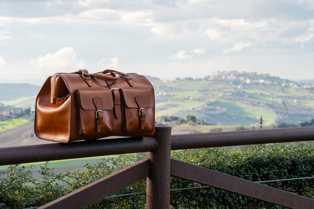 Wesley Deep Pocket Duffle in English Tan on a wooden fence overlooking Italian hills