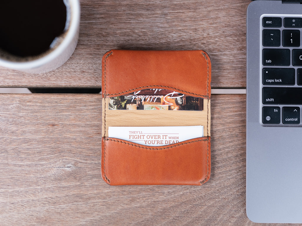 Slim Business Card Holder in English Tan, top-down view with cards inside next to a laptop