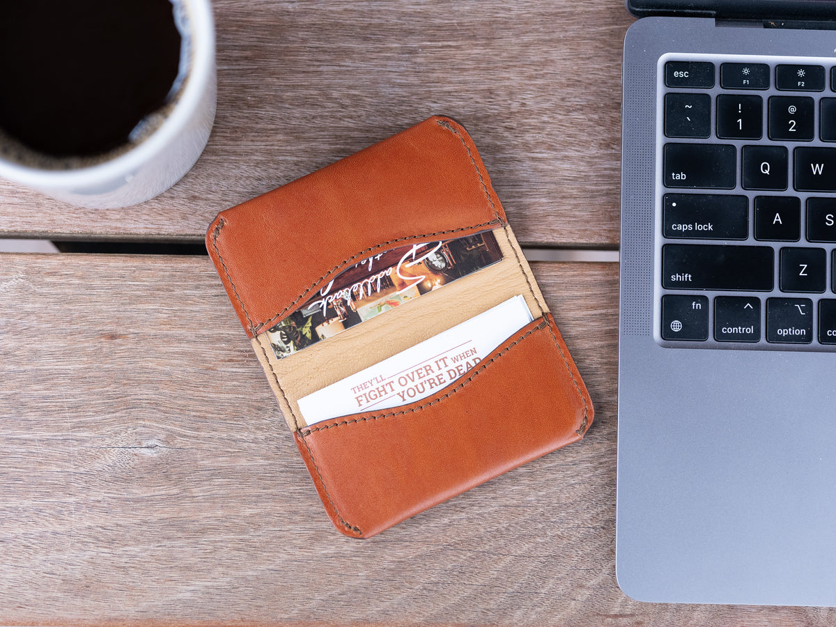 Slim Business Card Holder in English Tan with cards inside, on a wooden desk beside a laptop and coffee