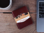 Slim Business Card Holder in Oxblood with cards inside, on a wooden desk beside a laptop and coffee